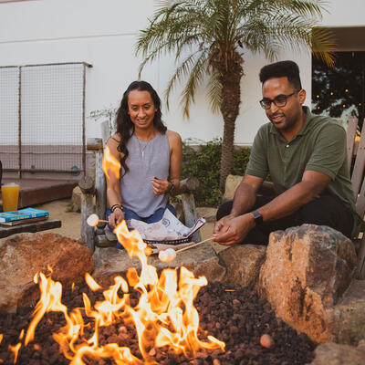 Exterior, a couple enjoys roasting marshmallows on a fire pit.