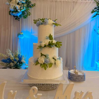 Three-tier textured white wedding cake decorated with blue and white flowers.