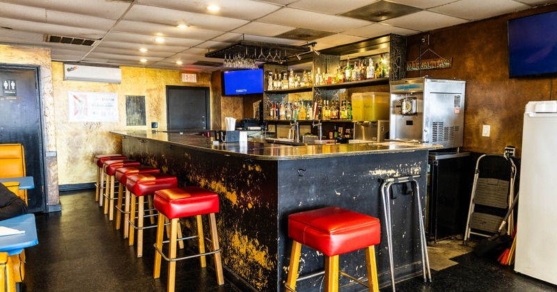 A cozy bar with a black, weathered counter and red cushioned stools
