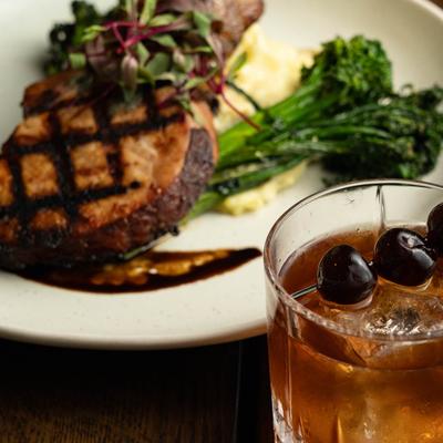 Grilled pork chop with mashed potatoes, broccolini, and a cocktail.