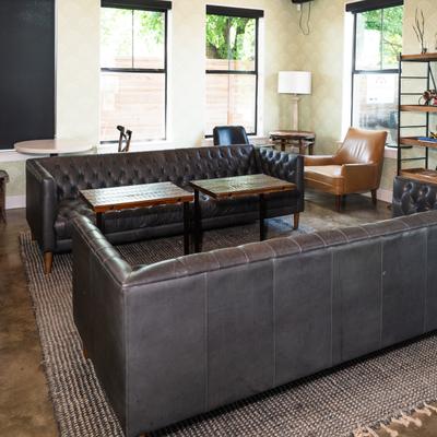 Stylish lounge with dark leather sofas, a tan armchair, and wooden tables on a textured rug.