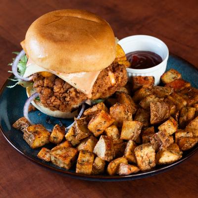 Crispy chicken sandwich with a side of roasted potatoes and a small dish of sauce.