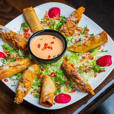 Taquitos platter with shredded lettuce, radishes, and dipping sauce.