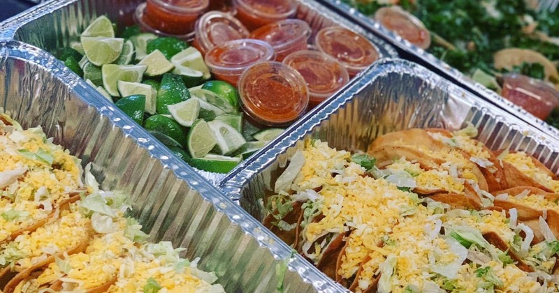 Catering dishes filled with tacos, lime wedges, and salsa containers