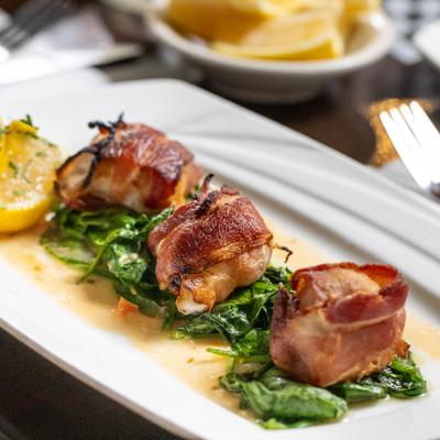 Bacon Wrapped Scallops served over spinach with a lemon wedge on the side.