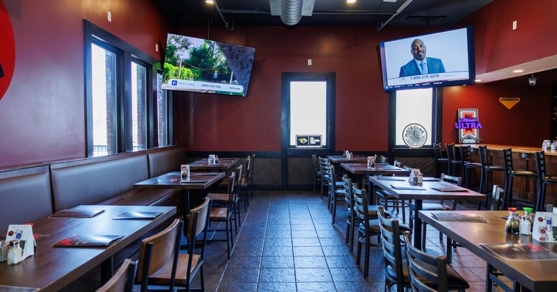 Interior with red walls, wooden tables and chairs, two TVs and neon signs.