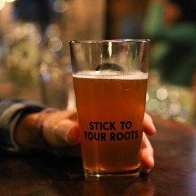 A person holding a glass of beer at a bar counter, close up.