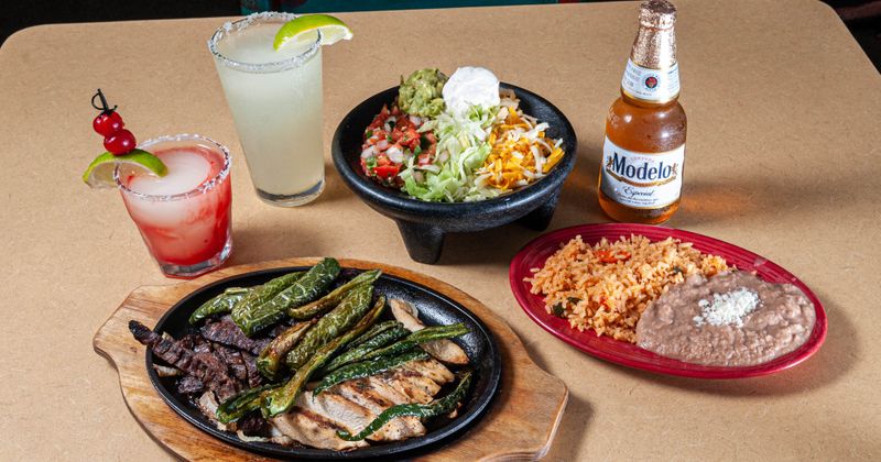 Beef and chicken fajitas plate served with side dishes, two cocktail and a beer