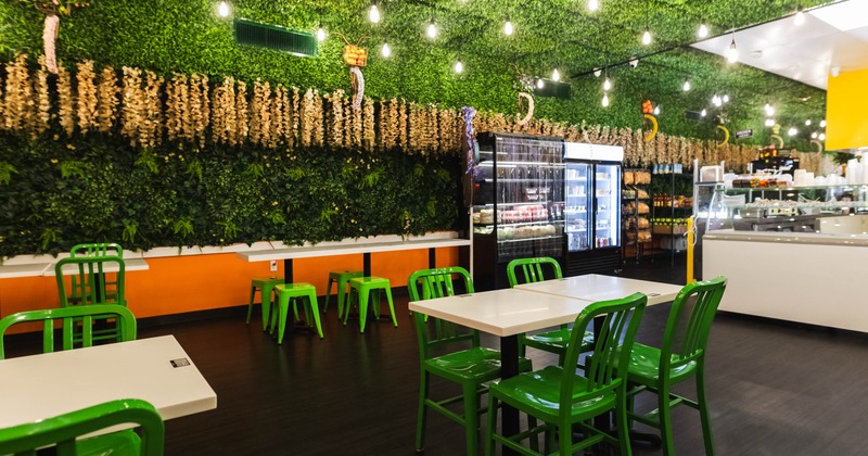 Inside of a cafe with green foliage on the ceiling and wall, green chairs, white tables