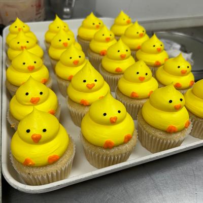 A tray of cupcakes topped with yellow frosting shaped like baby chicks.