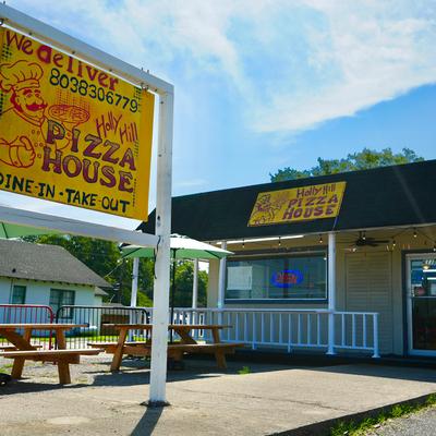 Holly Hill Pizza House exterior with signs, green umbrellas, and picnic tables.