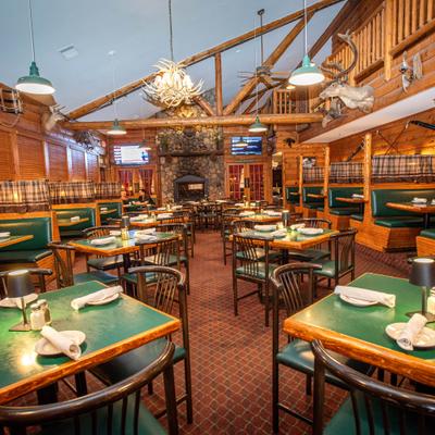 Rustic restaurant with wooden log walls, booths and green tables, set for dining.
