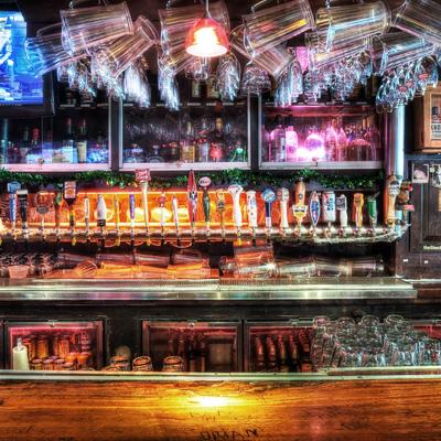 Bar interior with numerous beer taps, glass mugs hanging above, and a warmly lit wooden counter
