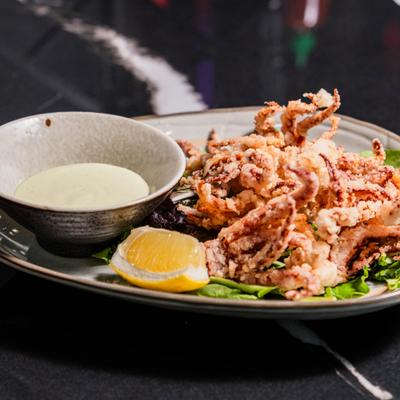 Crispy fried calamari served with a creamy sauce and a lemon wedge.