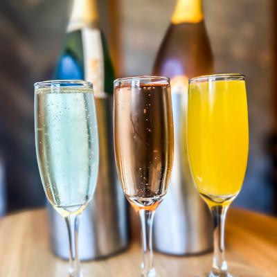 Three Mimosa cocktails, buckets with sparkling wine in the background.