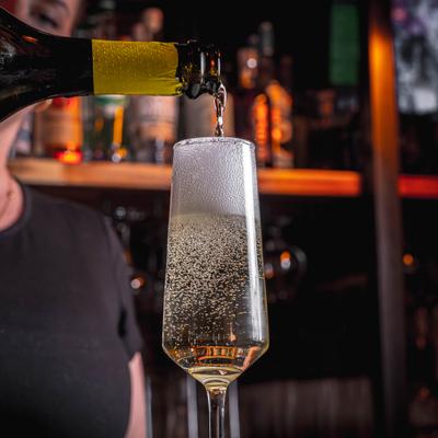 Sparkling wine poured into a tall glass at bar.