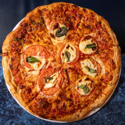 Margherita pizza featuring fresh mozzarella, sliced tomatoes, and basil leaves.