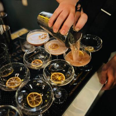 Bartender pours cocktail into coupe glasses, garnished with dried citrus slices.