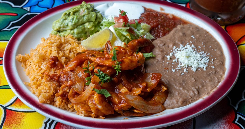 Spicy shrimp served on a plate with rice, beans, guacamole, and salsa