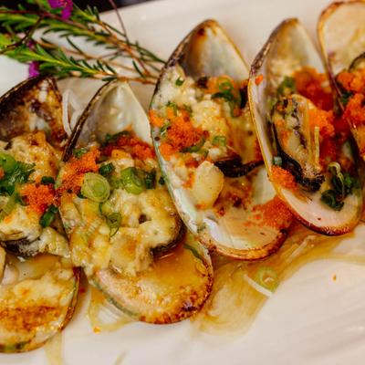 Baked mussels topped with sauce, herbs, and orange garnish.