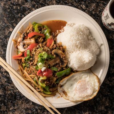 Stir-fry with mushrooms, rice, and a fried egg on a white plate with chopsticks.