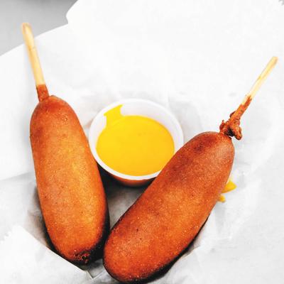 Two corn dogs with a side of dipping sauce.