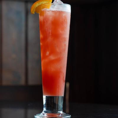 Ruby Relaxer cocktail served in a Pilsner  glass with an orange slice garnish.