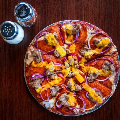 Pizza topped with pepperoni, sausage, red onion rings, and strips of sharp cheddar.