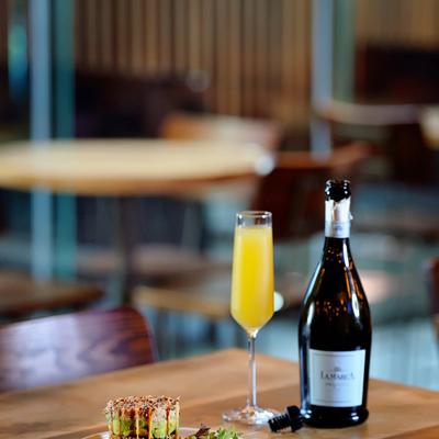 A bottle of champagne and a mimosa on a wooden table.