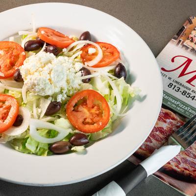 Close up of a plate of Greek salad and  the restaurant menu on the table.