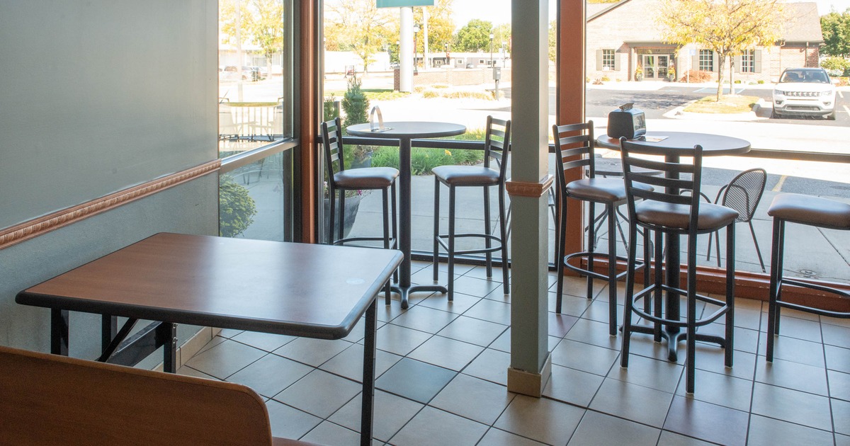 Interior of a café with tables, bar stools, large windows, and a view of a street