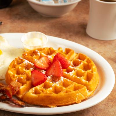 Waffle with strawberries, bacon, fried eggs, and coffee.