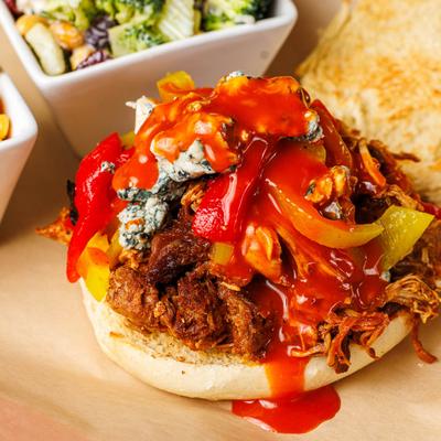 Buffalo Chicken Sammy with sides of Cajun corn and broccoli salad, close up.
