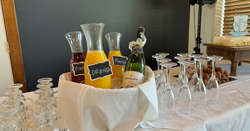Ice bucket with carafes of assorted juices and a bottle of champagne surrounded by glassware