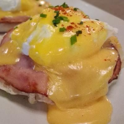 A close-up of eggs Benedict featuring Canadian bacon, hollandaise sauce, and chives.