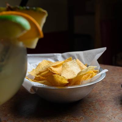 A bowl of tortilla chips with a tropical cocktail in the foreground.