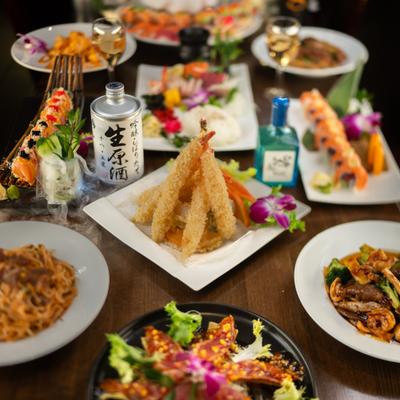 Table filled with assorted sushi, noodles, tempura, and drinks.