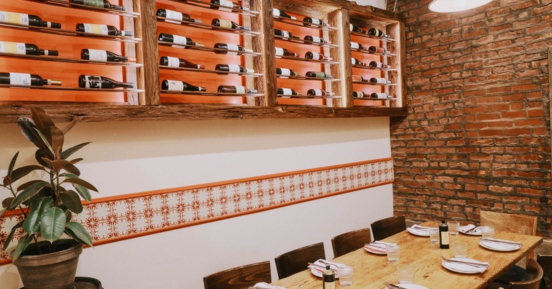Dining table set for guests with wooden wine racks filled with bottles above