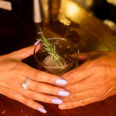 Two hands gently wrap around a cocktail garnished with rosemary.
