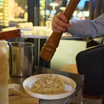 A plate of pasta being seasoned with pepper from a large wooden grinder.