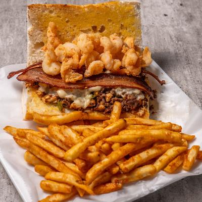 Sandwich with ground beef, bacon, and shrimp, served with fries.
