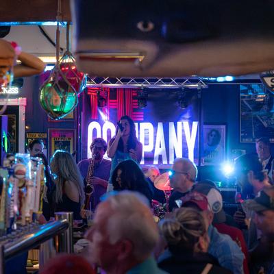 Crowded bar area with a band performing on a stage.