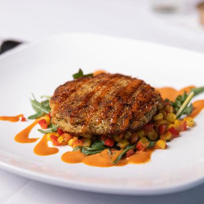 Crab Cake served with roasted peppers and corn, drizzled with sauce.