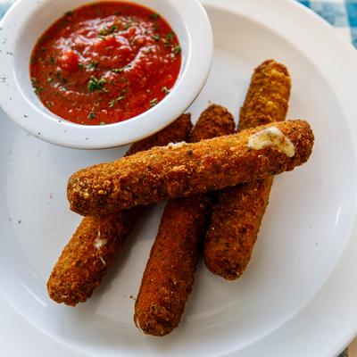Four mozzarella sticks served on a white plate with a bowl of tomato sauce.