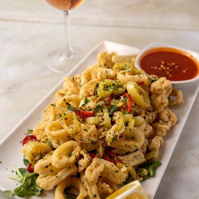 Plate of fried calamari topped with pepperoncini and served with dipping sauce.