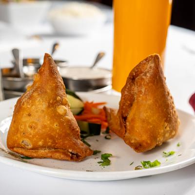 Vegetable samosas on a plate with fresh vegetables, Mango Lassi is in the background.