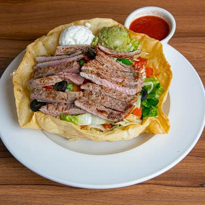 Steak salad served in a tortilla shell with guacamole and sour cream, side of red salsa.