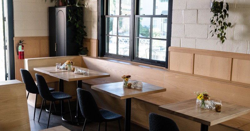 Cozy interior with wooden tables and black chairs; small flower arrangements and pendant lights
