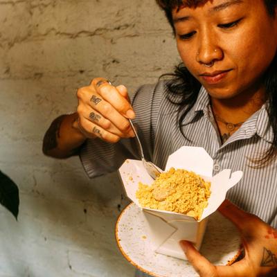 Person eating noodles from a takeout box.
