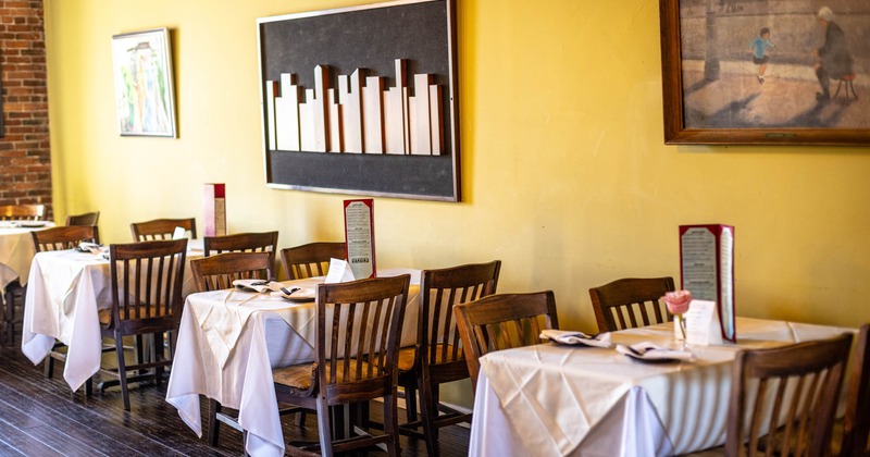 Interior, tables and chairs ready for guests, yellow wall with paintings on the right